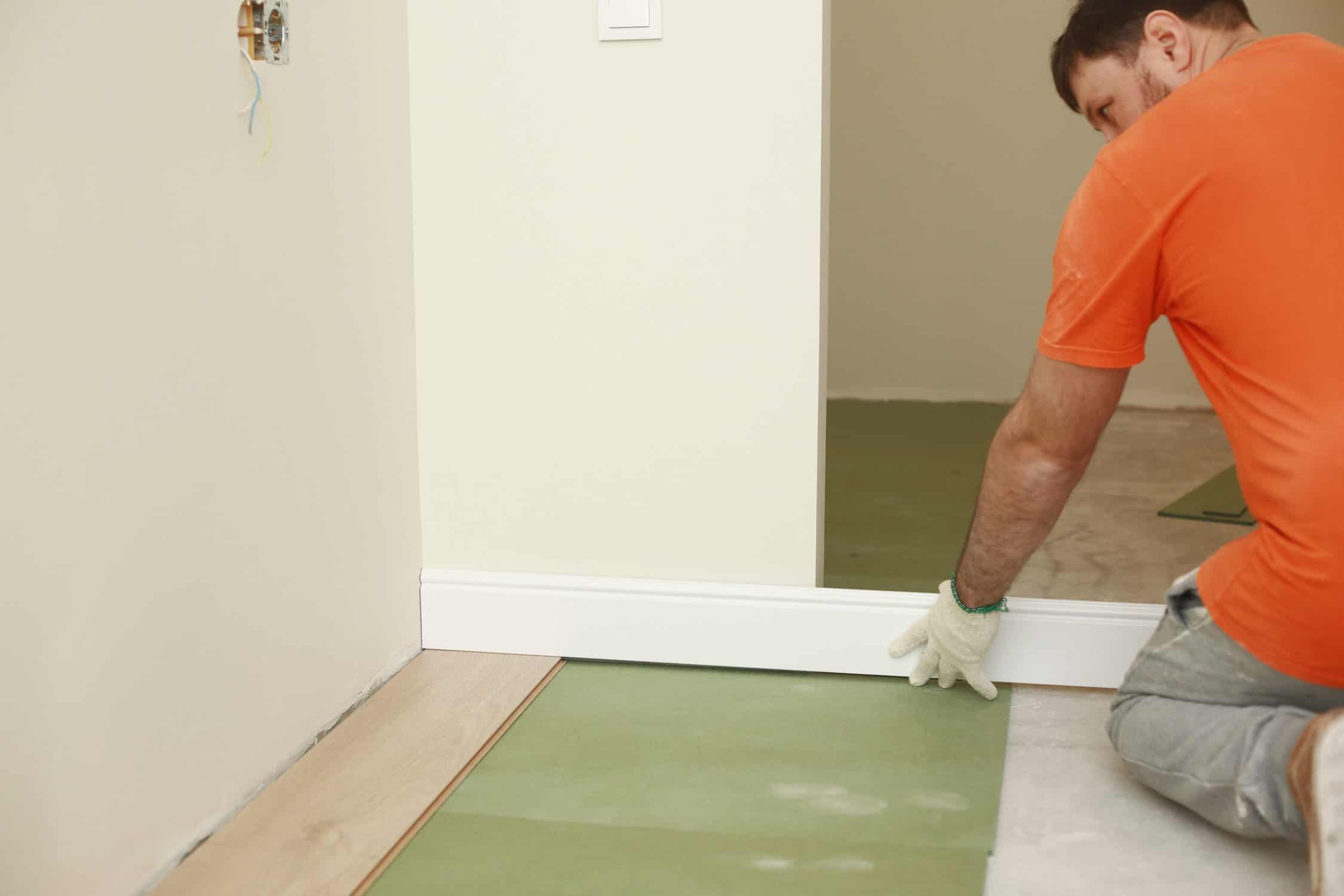 the worker installs plinths in the apartment. Installing a white plastic skirting board on a laminate - adjusting and trimming